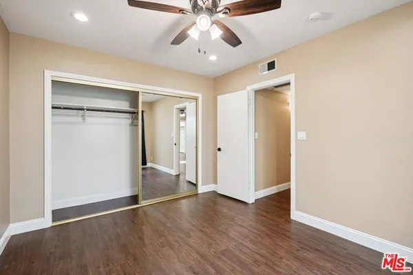 a view of an empty room with wooden floor and a ceiling fan