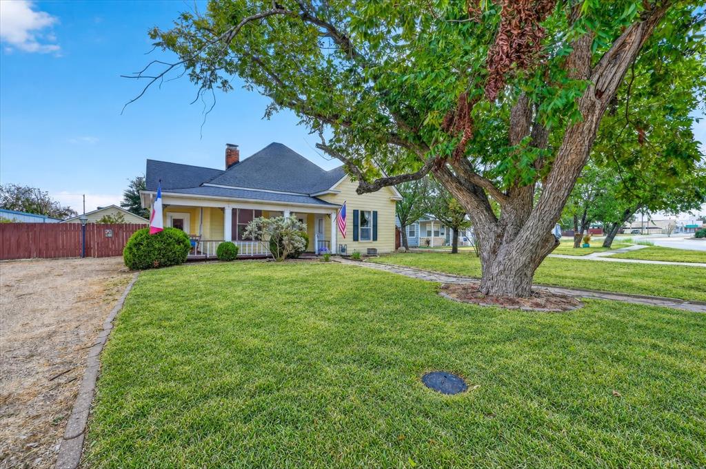 304 East Main Street Itasca, TX 76055 - Photo 2 of 38 Yellow exterior featuring a covered porch with white columns, dark roof, and a red brick chimney