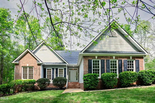 a view of a house with brick walls and a yard with plants and large trees
