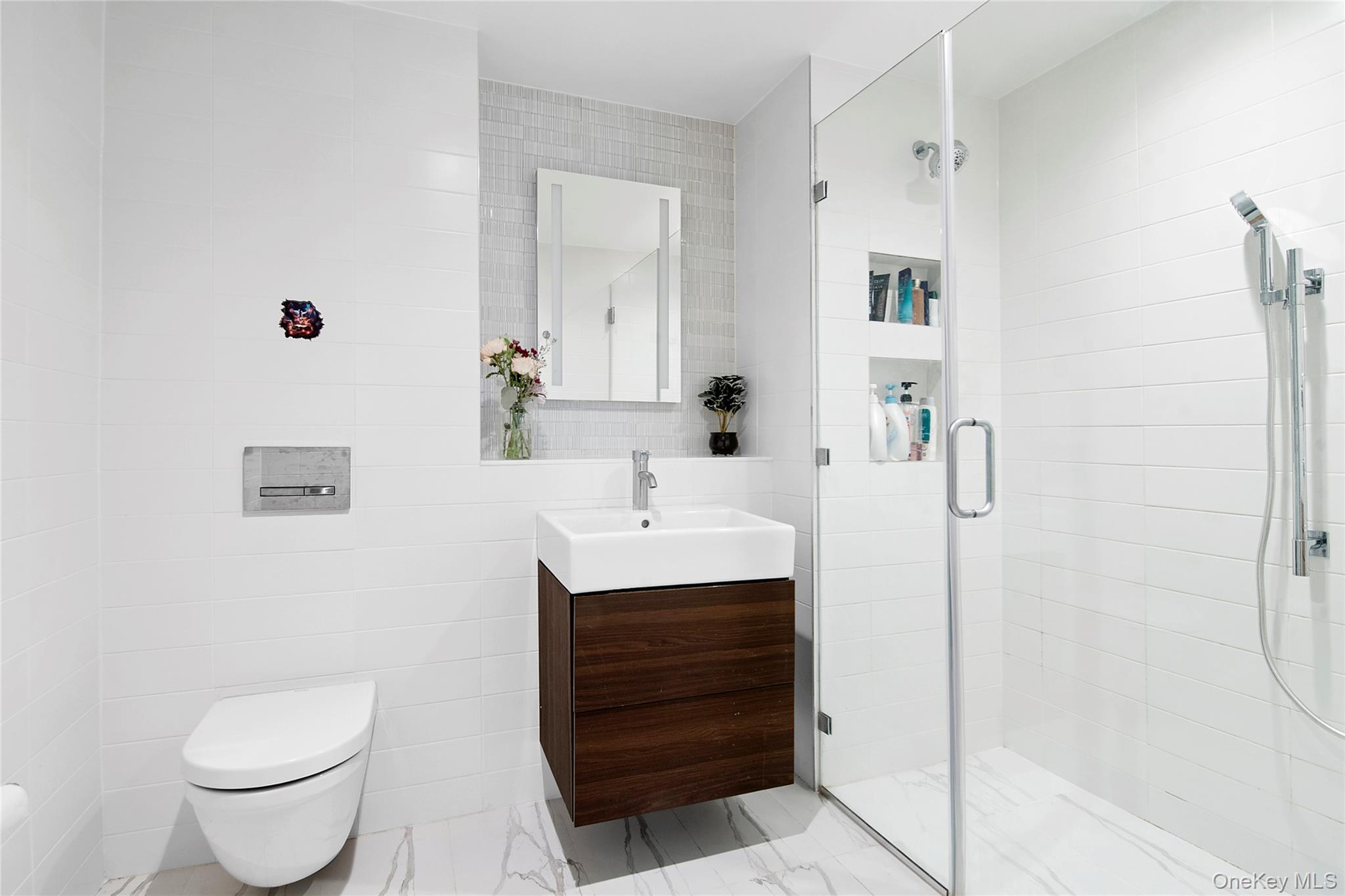 1064 Hancock Street, Unit 101 Brooklyn, NY 11221 - Photo 4 of 9 Contemporary bathroom featuring heated floors, a floating wood-finish vanity with a vessel sink, a mirrored medicine cabinet, a frameless glass shower enclosure with built-in shelving, a wall-mounted toilet, and large format tile flooring