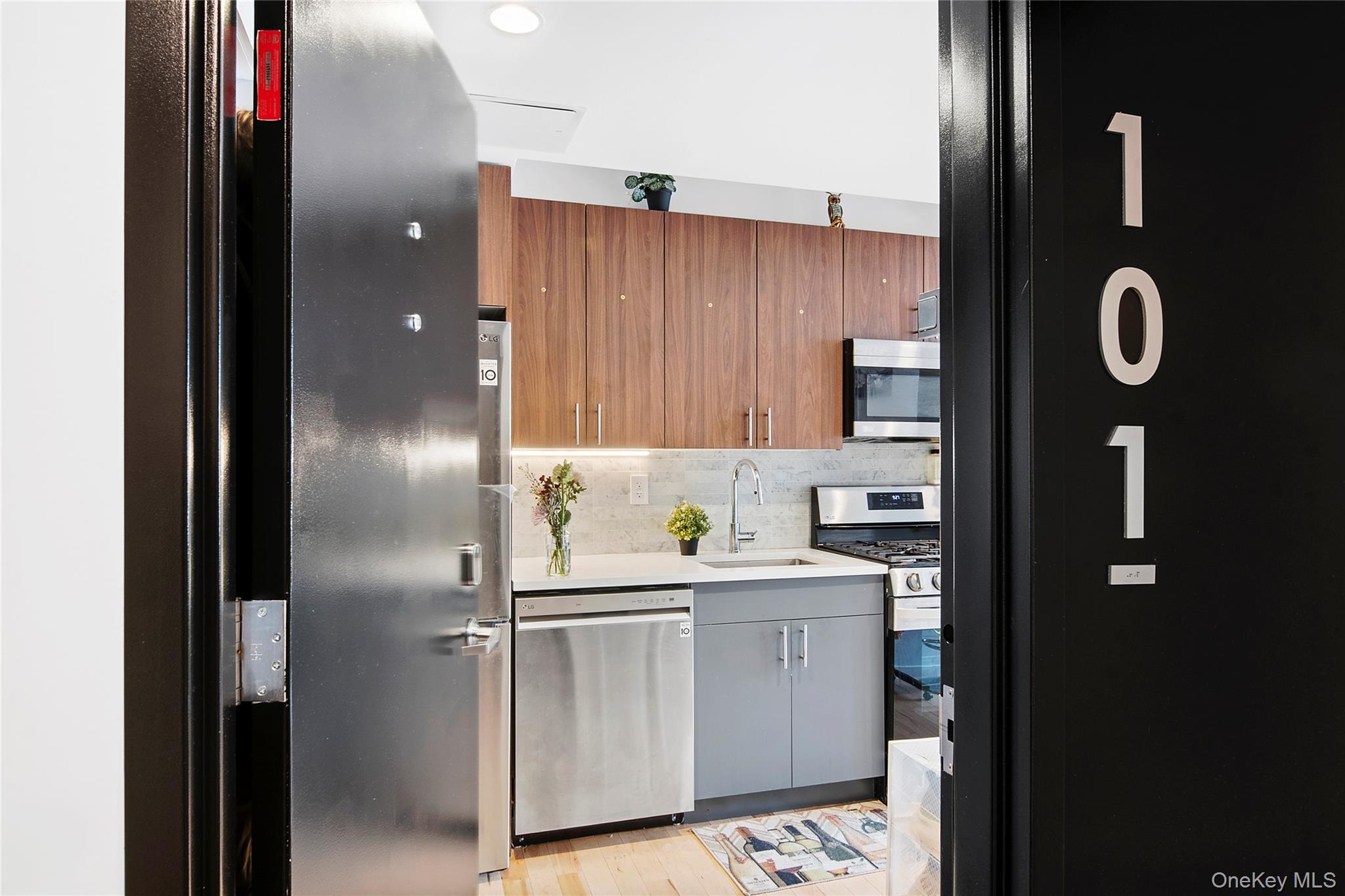 1064 Hancock Street, Unit 101 Brooklyn, NY 11221 - Photo 6 of 9 Compact kitchen featuring modern wood-finish cabinetry, light-toned countertop, stainless steel appliances, and a gas range