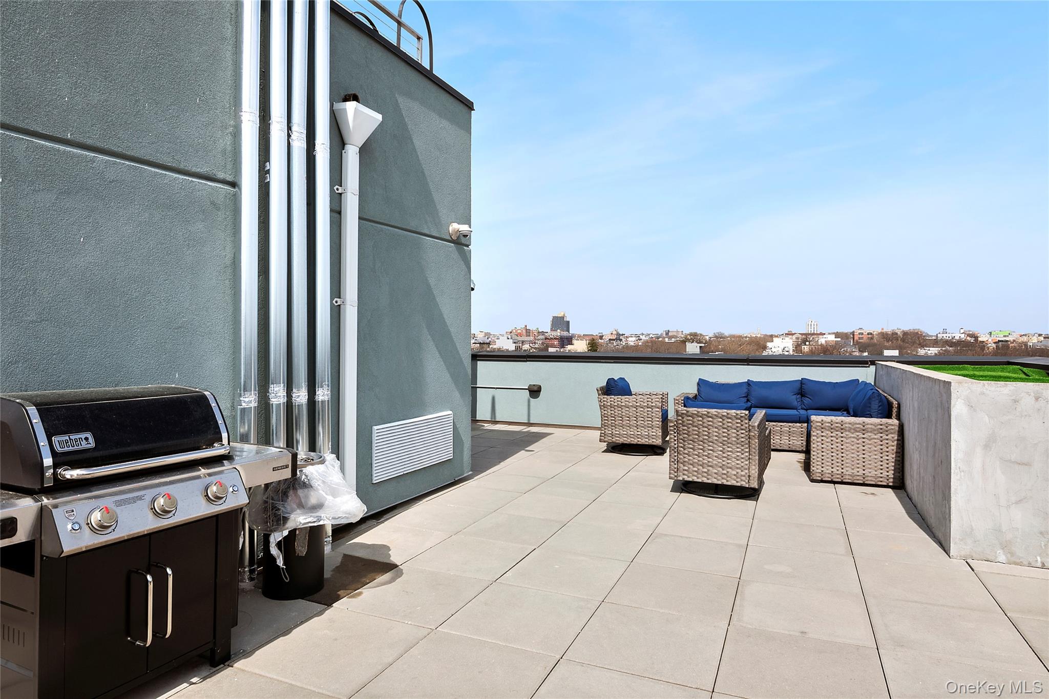 1064 Hancock Street, Unit 101 Brooklyn, NY 11221 - Photo 7 of 9 Expansive rooftop terrace featuring large format paver flooring, a perimeter wall with artificial turf accent, a flat roofline, and a cityscape horizon