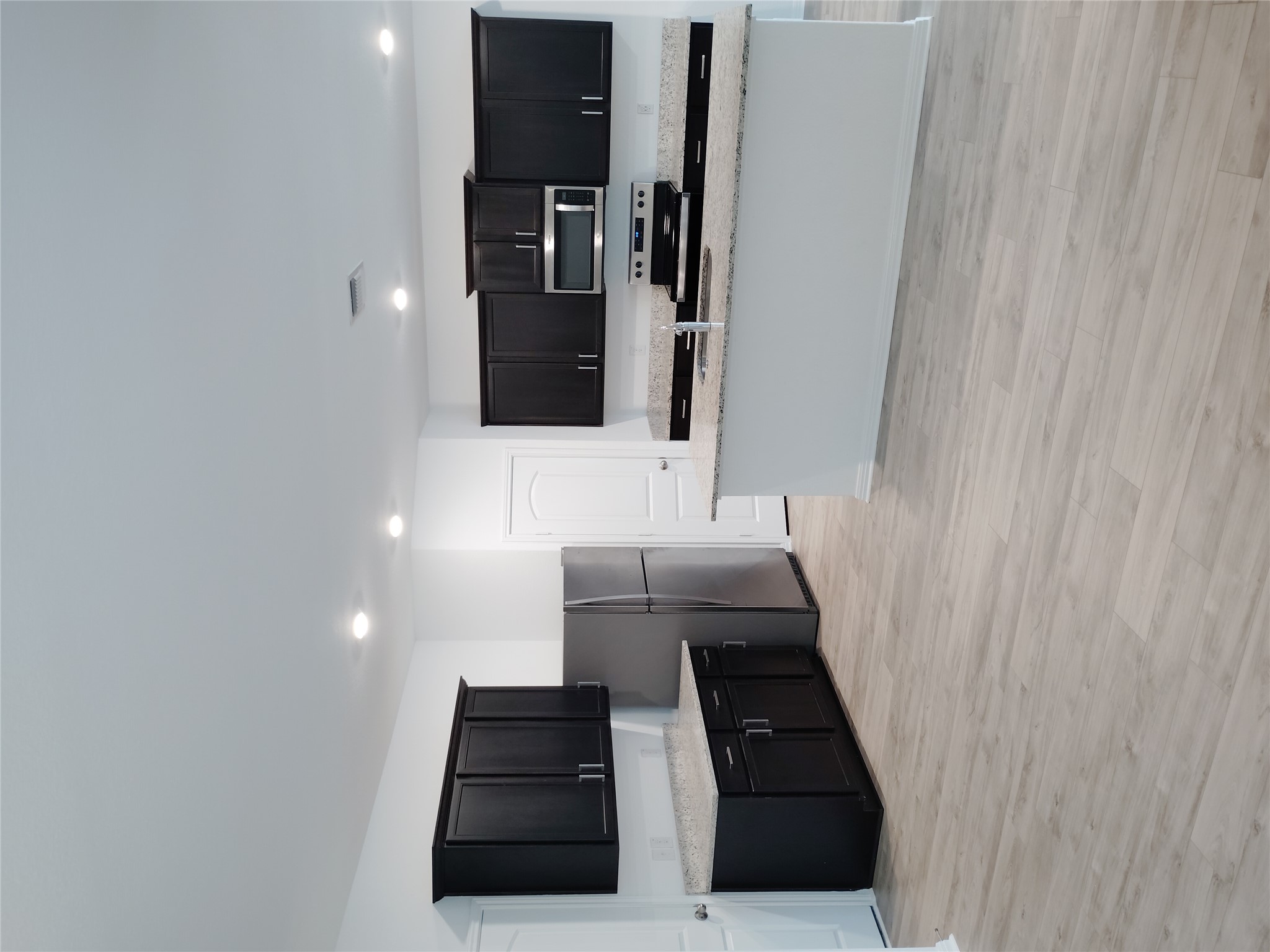 14024 Prairie Schooner Pass Elgin, TX 78621 - Photo 7 of 20 Open concept kitchen featuring dark wood cabinetry, light-colored speckled countertops, stainless steel appliances, and a central island with an integrated sink