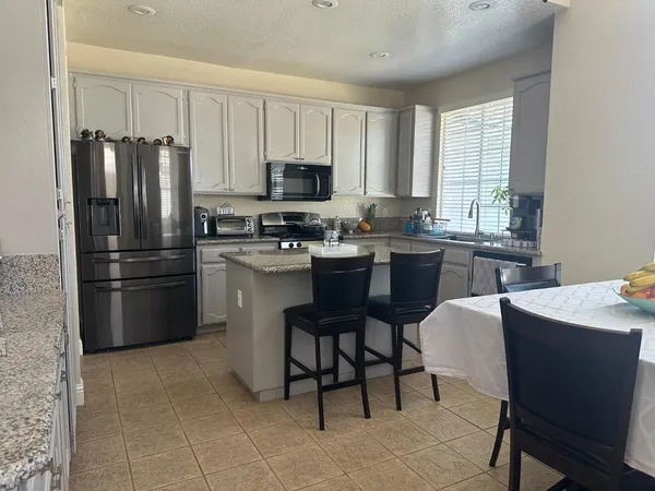 a kitchen with stainless steel appliances granite countertop a refrigerator a sink a stove a dining table and chairs