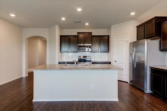 a kitchen with stainless steel appliances granite countertop a refrigerator a sink a stove a microwave and wooden floor