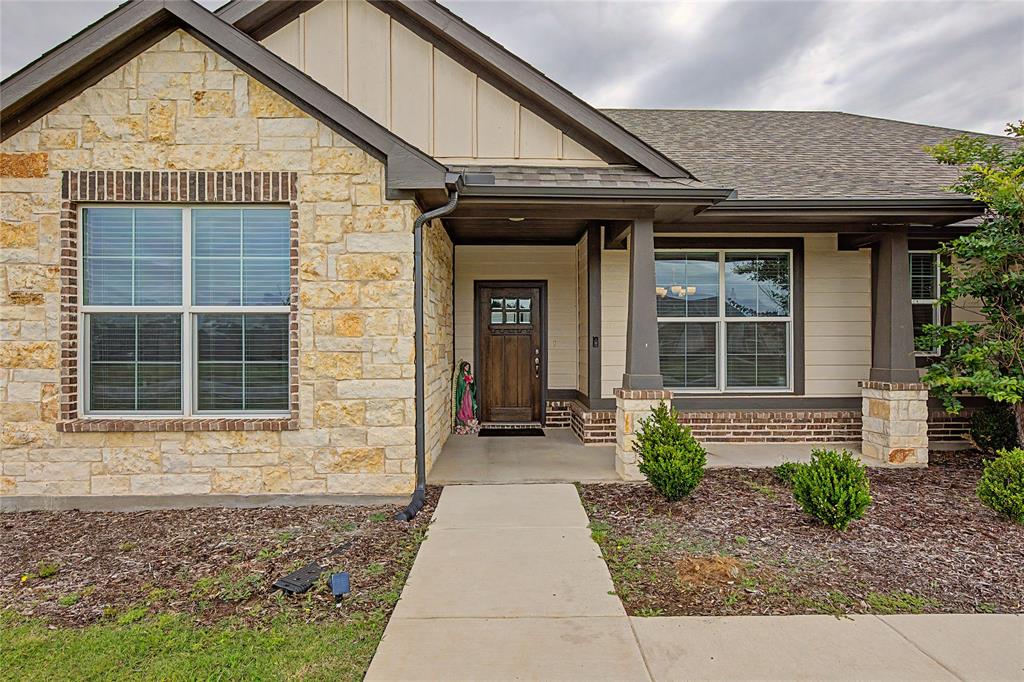 185 Chester Road Springtown, TX 76082 - Photo 8 of 40 Crafted stone and brick exterior featuring a covered entry, decorative gables, a wood-finish entry door with glass inserts, and a concrete pathway