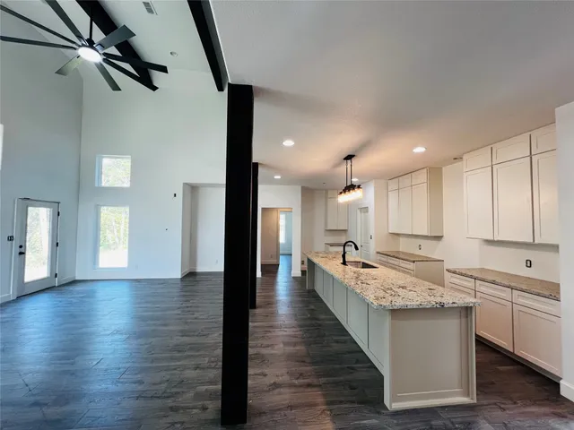 a large kitchen with kitchen island a stove a sink a refrigerator and white cabinets with wooden floor