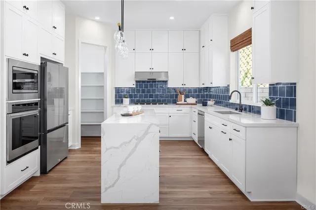 a large kitchen with stainless steel appliances a large counter top a stove a refrigerator and a window