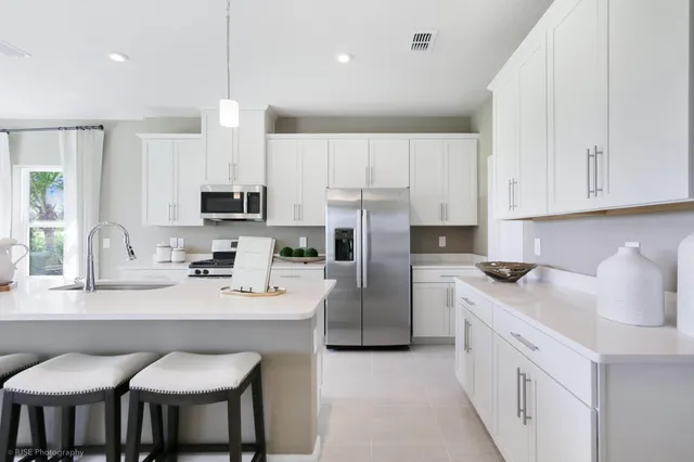 a kitchen with stainless steel appliances a sink a stove a refrigerator cabinets and chairs
