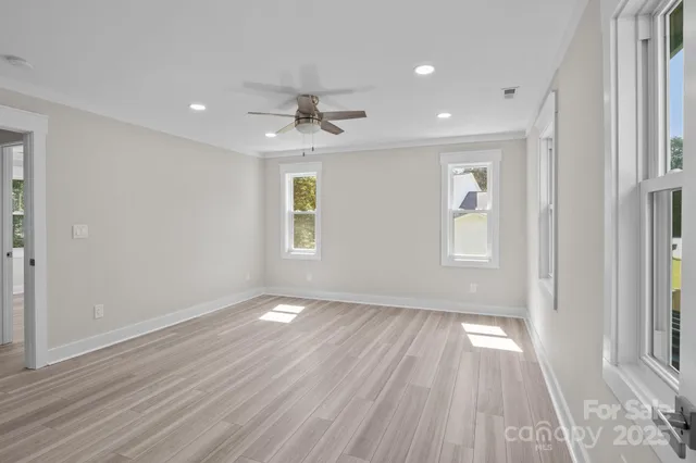 an empty room with wooden floor ceiling fan and windows