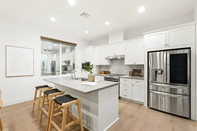 a kitchen with stainless steel appliances kitchen island granite countertop a stove a sink a refrigerator and white cabinets with wooden floor