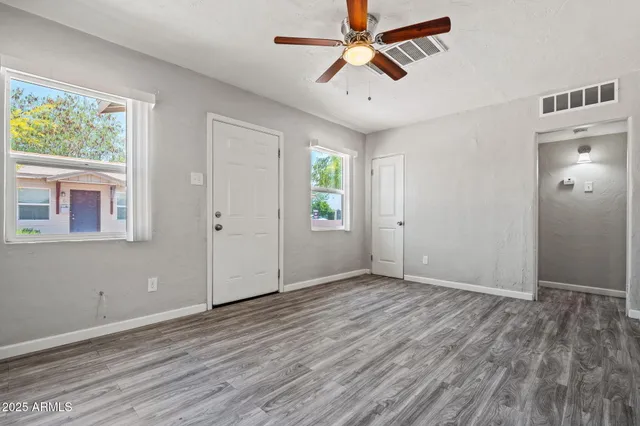 an empty room with wooden floor chandelier fan and windows