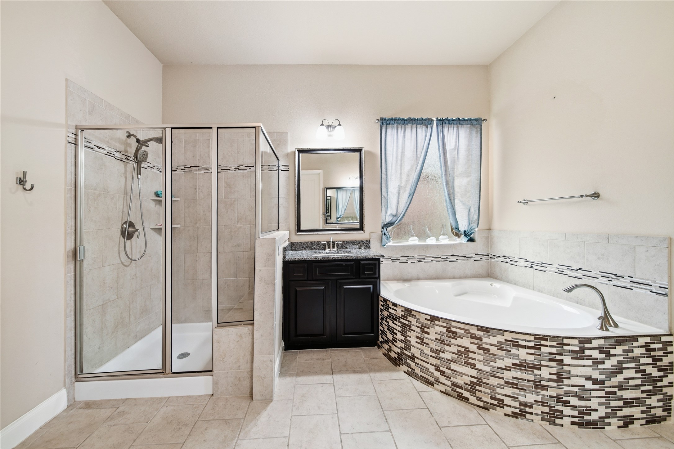 5303 Mesquite Willow Lane Rosharon, TX 77583 - Photo 18 of 32 This primary bathroom features a spacious design with a glass-enclosed shower, a large corner bathtub with decorative tile, a single-sink vanity with a mirror, and a window with natural light.