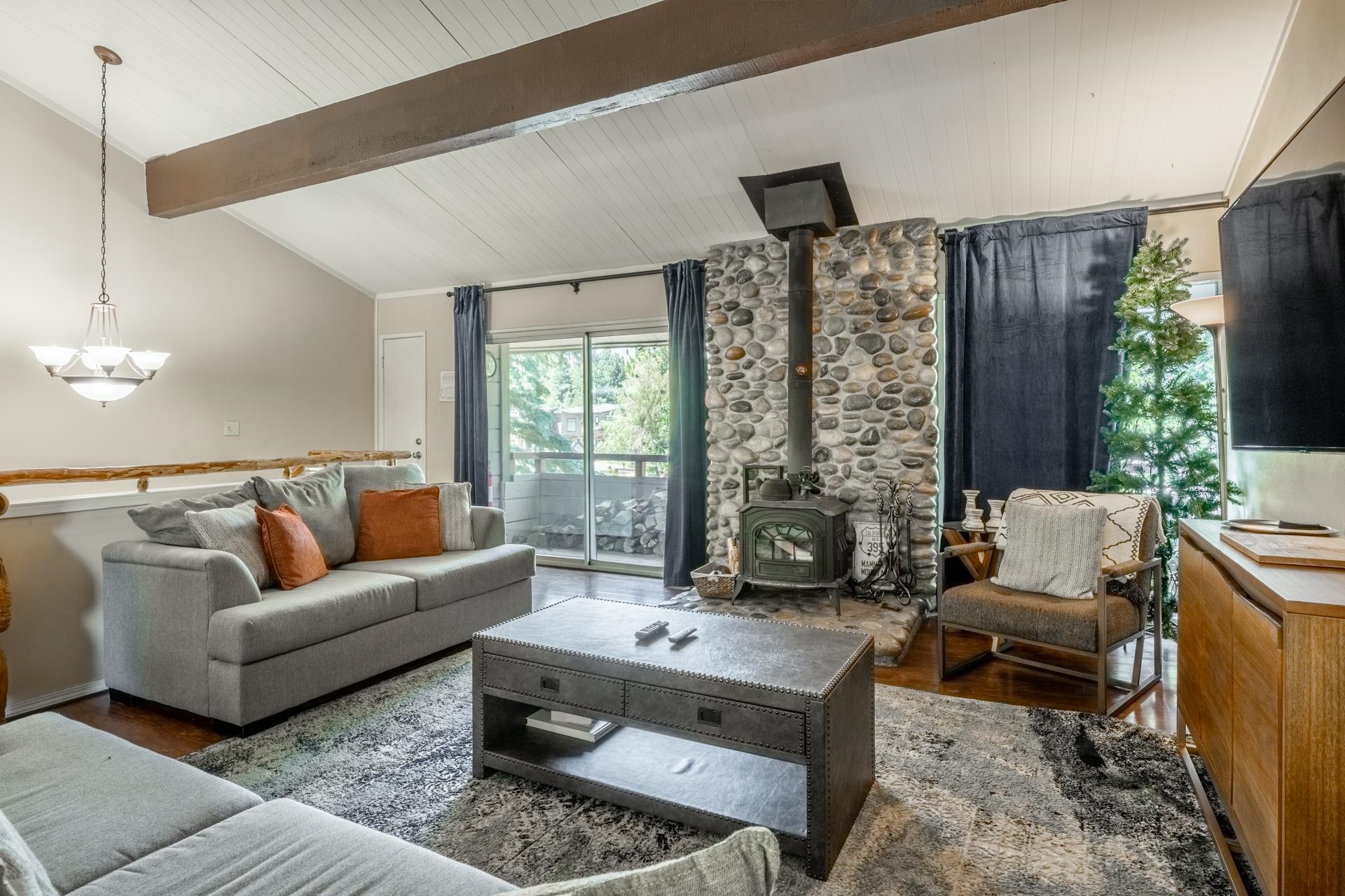 165 Old Mammoth Road, Unit 3 Mammoth Lakes, CA 93546 - Photo 2 of 48 Living area featuring a stone wood-burning stove, vaulted ceiling with exposed beam, wood-finish flooring, and sliding glass doors