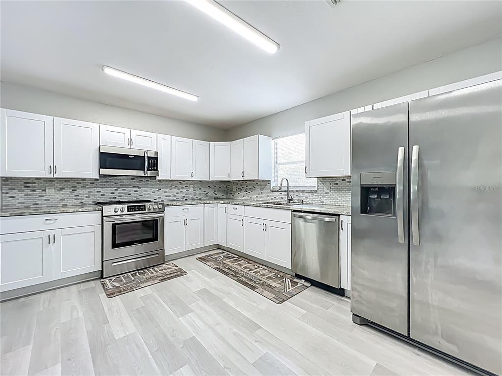 12368 Killian Street Spring Hill, FL 34609 - Photo 9 of 25 a kitchen with granite countertop a refrigerator oven a sink and white cabinets