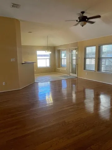 an empty room with wooden floor chandelier and windows