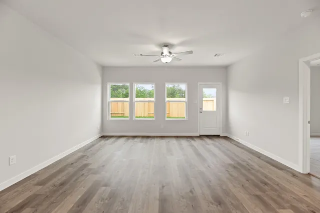 an empty room with wooden floor chandelier fan and windows
