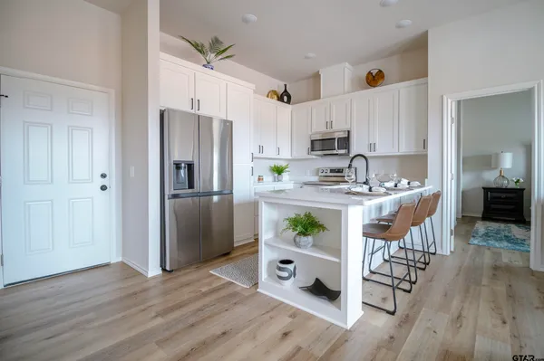 a kitchen with stainless steel appliances a stove a refrigerator a sink a dining table and chairs with wooden floor