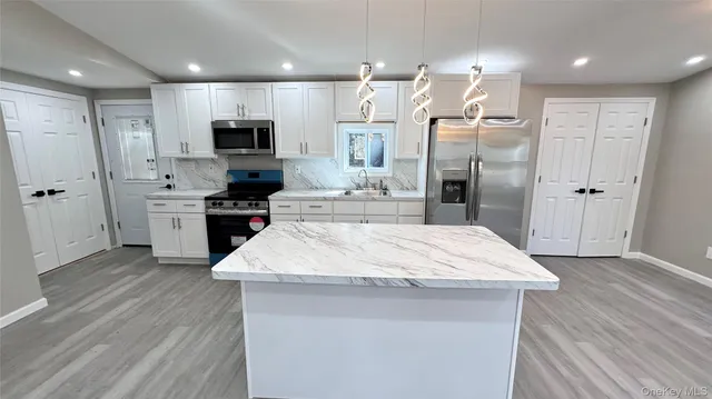 a room with stainless steel appliances kitchen island granite countertop a refrigerator a sink a stove and oven