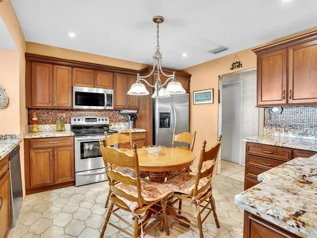 a kitchen with stainless steel appliances granite countertop a stove top oven a refrigerator a sink dishwasher a dining table and chairs with wooden floor