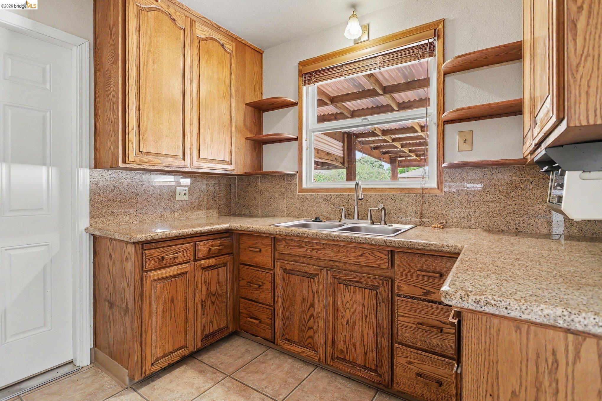 249 Madison Avenue Bay Point, CA 94565 - Photo 8 of 18 Kitchen featuring wood cabinetry with ample storage, a double basin stainless steel sink, natural stone countertops, a coordinated stone backsplash, and tile flooring