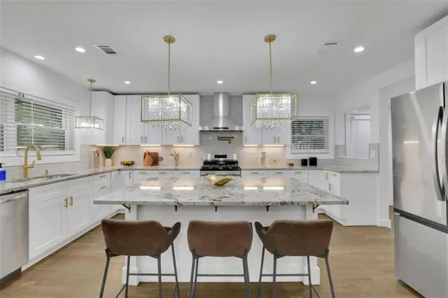 a kitchen with stainless steel appliances granite countertop a stove top oven a refrigerator a sink and chairs