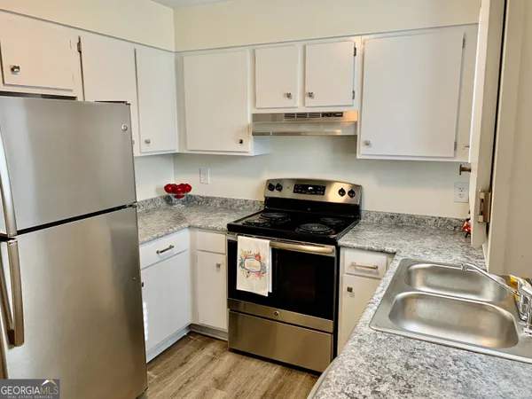 a kitchen with granite countertop a refrigerator sink stove and white cabinets