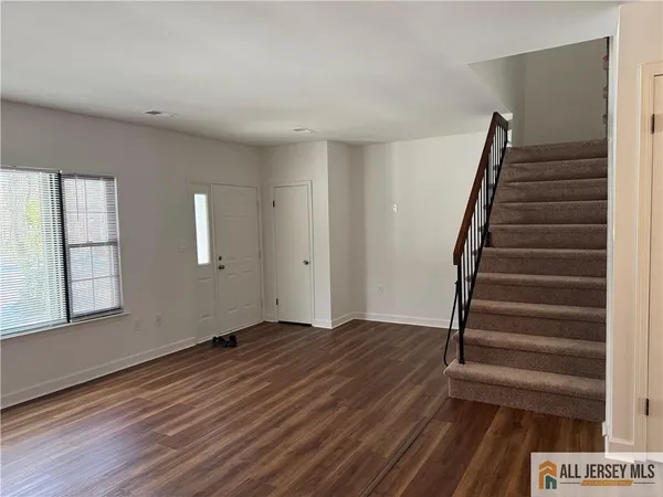 a view of an empty room with wooden floor and stairs
