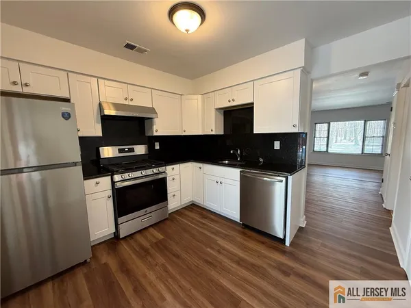 a kitchen with stainless steel appliances a refrigerator stove a sink and white cabinets with wooden floor