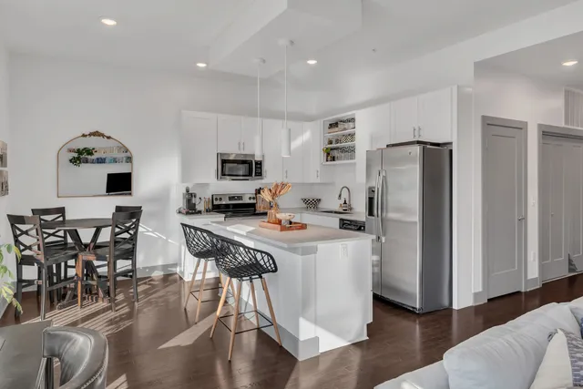 a kitchen with stainless steel appliances a refrigerator a stove a sink a dining table and chairs with wooden floor