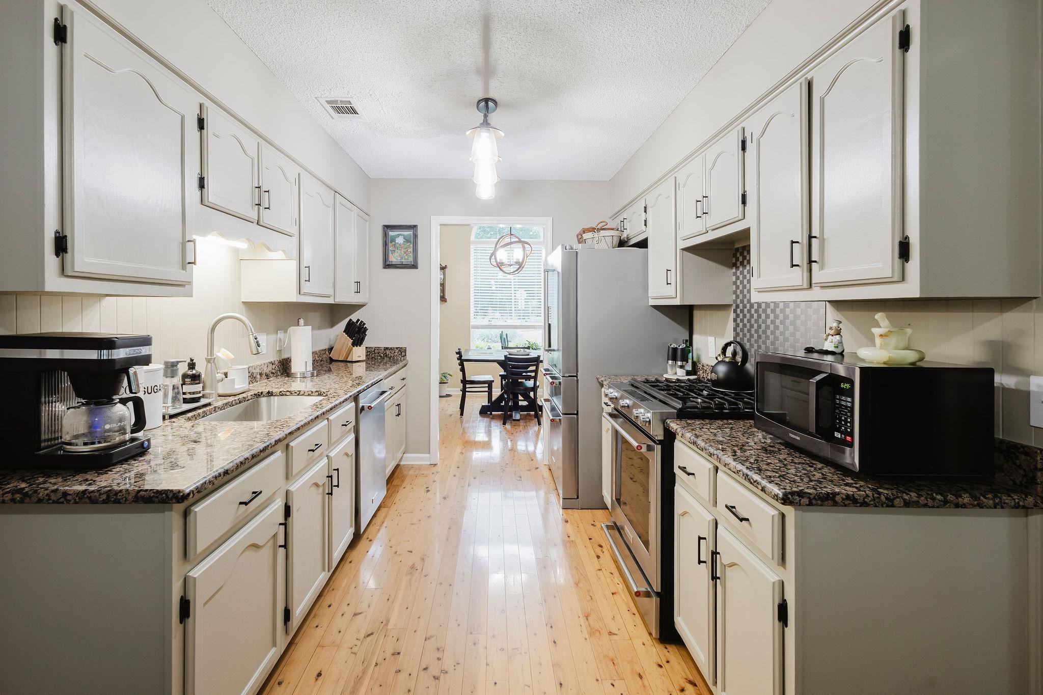 305 Great Falls Road Collierville, TN 38017 - Photo 5 of 23 Galley kitchen featuring light wood-finish flooring, white cabinetry, dark speckled countertops, and a stainless steel refrigerator