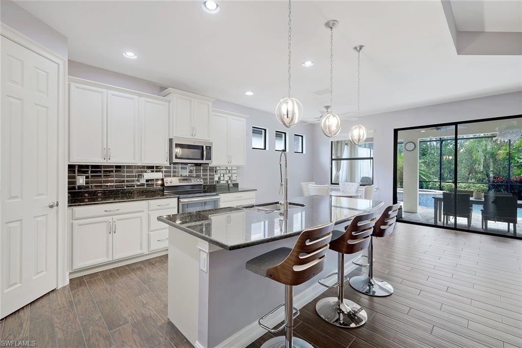 14374 Tuscany Pointe Trail Naples, FL 34120 - Photo 6 of 22 a kitchen with granite countertop stainless steel appliances a stove a sink a oven a dining table and chairs with wooden floor