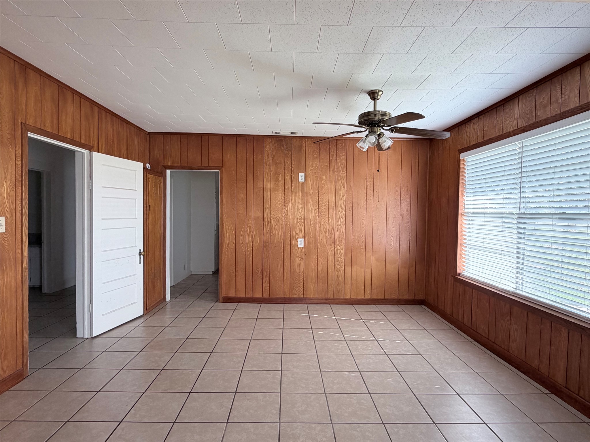 500 Greasy Bend Road Smithville, TX 78957 - Photo 4 of 21 Interior room featuring wood paneling, tiled flooring, a ceiling fan with integrated lighting, and a window with blinds