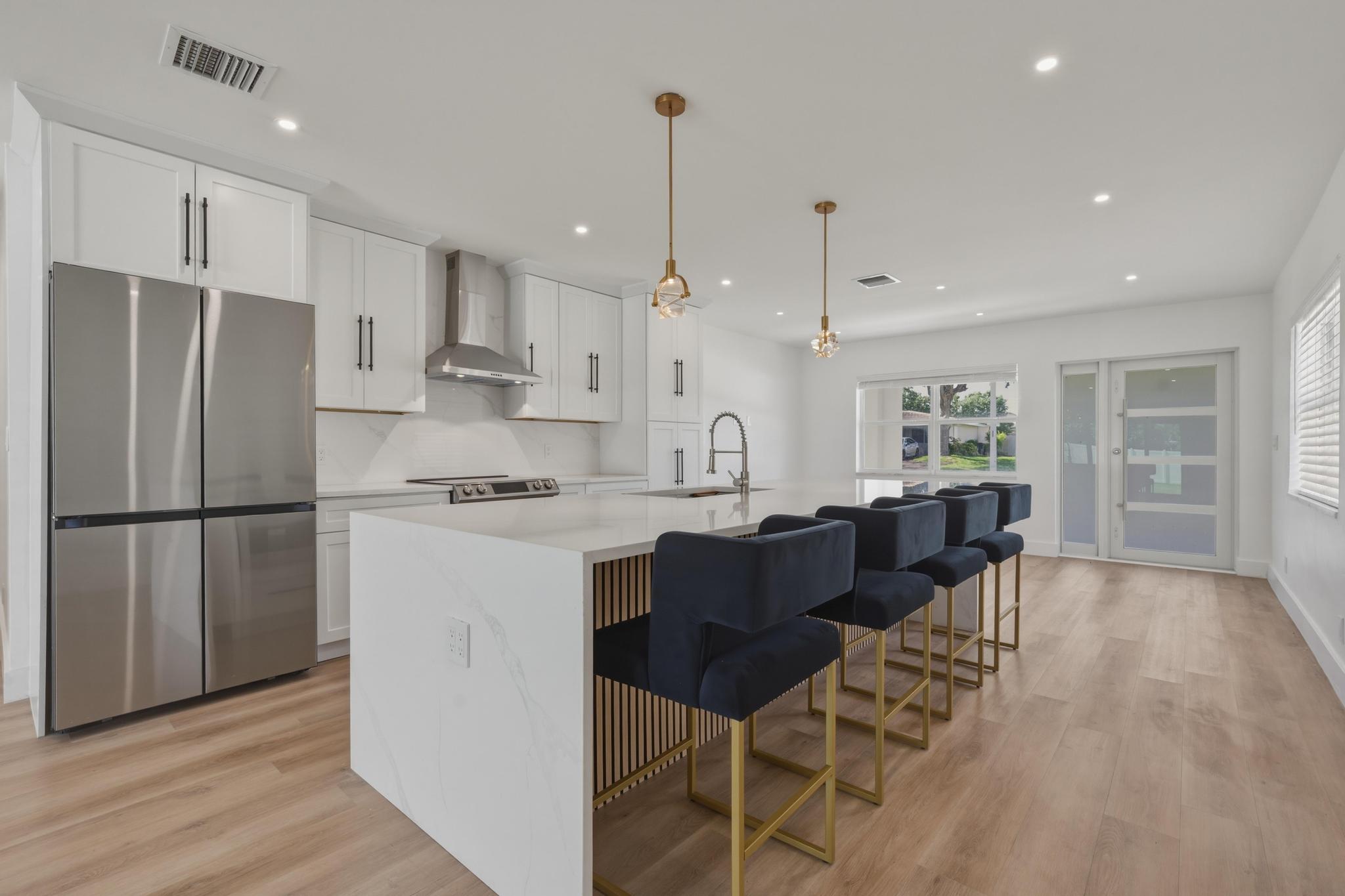 a kitchen with stainless steel appliances kitchen island granite countertop a refrigerator a stove a sink a dining table and chairs with wooden floor