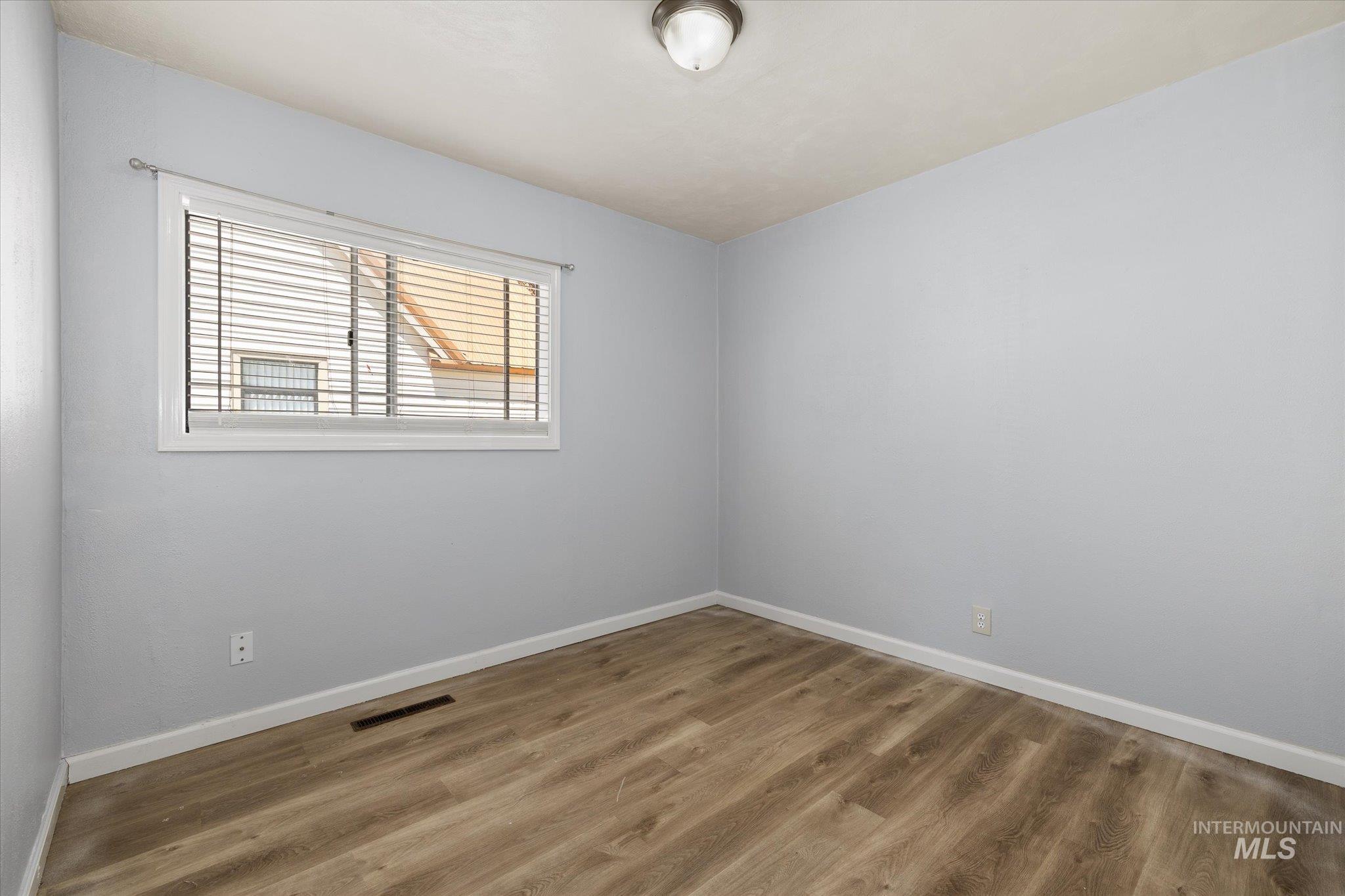 918 West 3rd Street Weiser, ID 83672 - Photo 12 of 36 Room featuring light blue walls, wood-finish flooring, white baseboards, and a window with horizontal blinds
