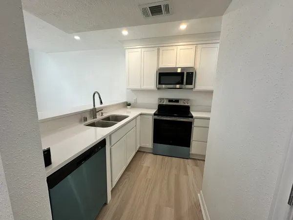 a kitchen with a sink dishwasher a stove top oven a refrigerator with wooden floor and cabinets