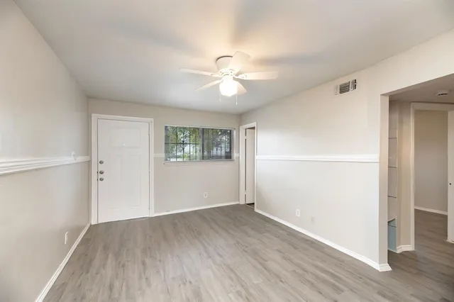 an empty room with wooden floor ceiling fan and windows