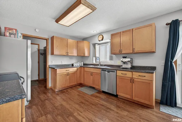 a kitchen with granite countertop wooden floors stainless steel appliances a sink and a window