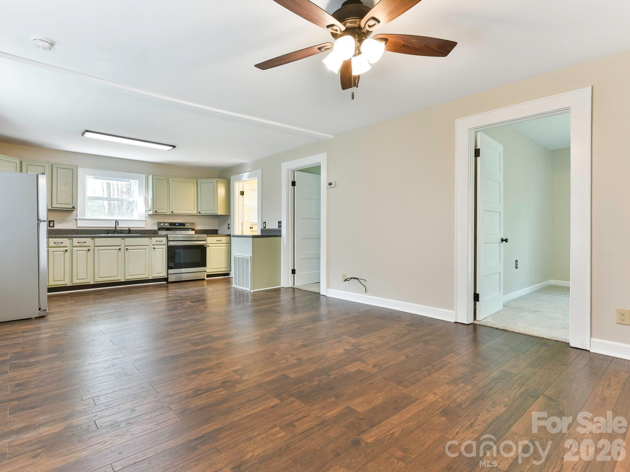 8202 Karriker Road Kannapolis, NC 28081 - Photo 5 of 12 an empty room with wooden floor a ceiling fan a kitchen view and a window