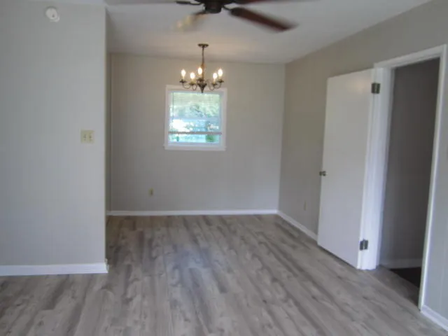 an empty room with wooden floor chandelier and windows