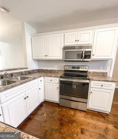 a kitchen with granite countertop white cabinets appliances and a window