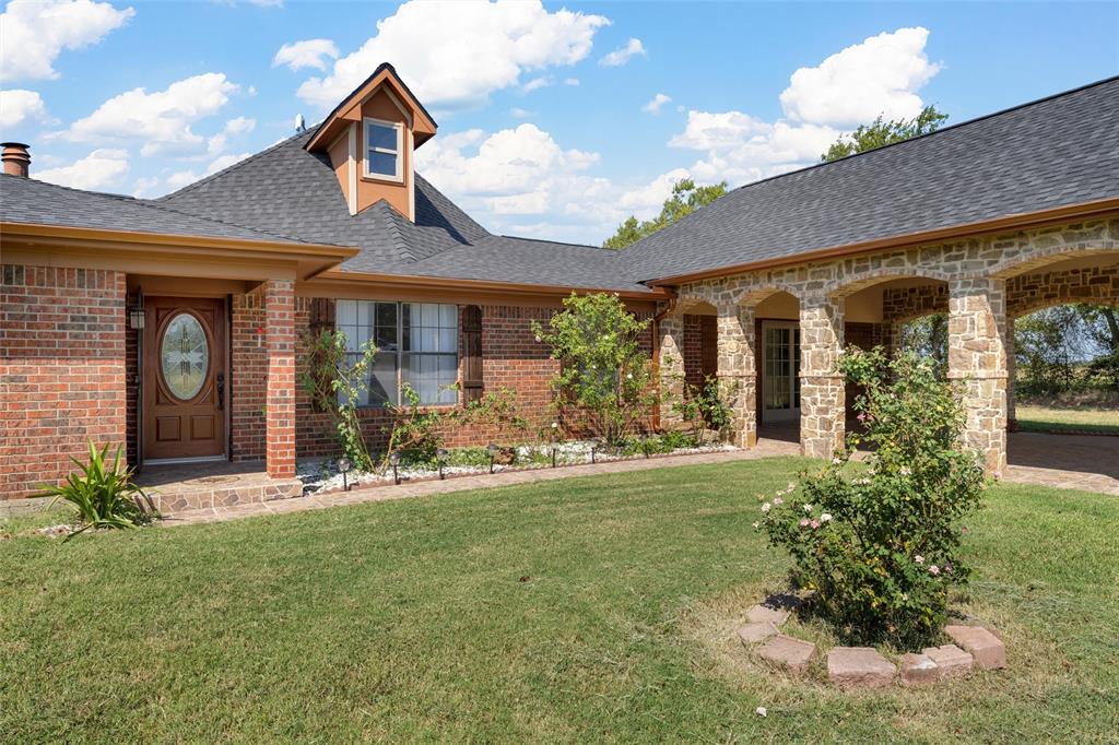 3433 West Tours Road West, TX 76691 - Photo 6 of 40 View of exterior entry featuring roof with shingles, a yard, and brick siding