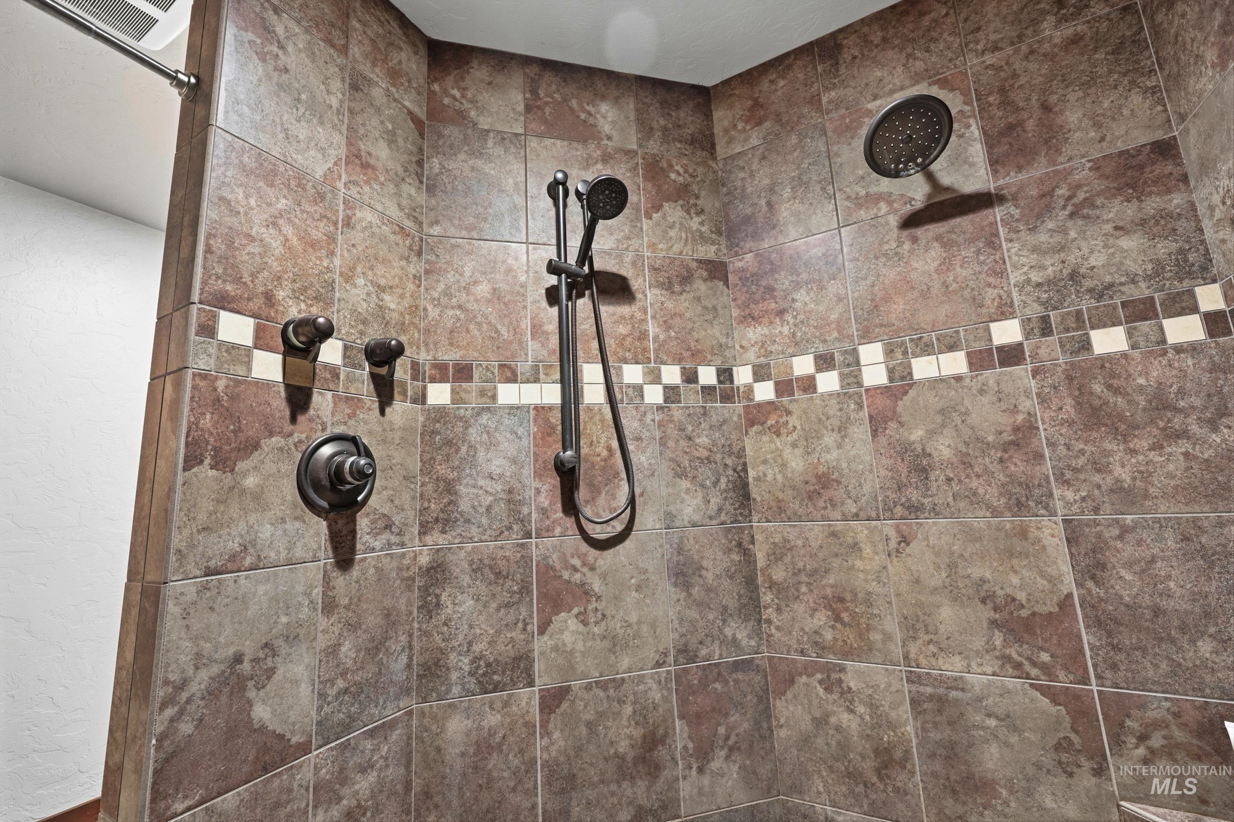 339 Airport Road Weiser, ID 83672 - Photo 24 of 49 Shower enclosure featuring large format stone-look tiles, a decorative mosaic tile accent band, a fixed rain shower head, and a handheld shower fixture