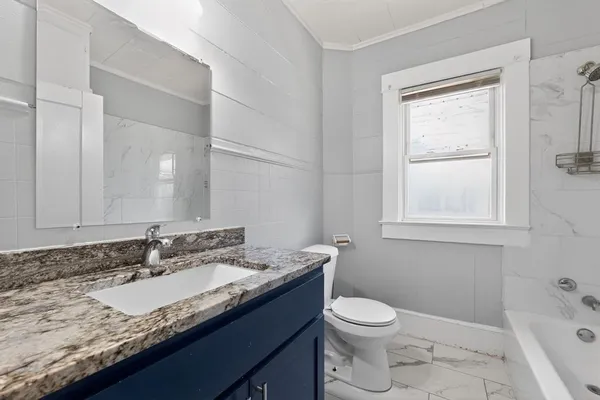 a bathroom with a granite countertop sink toilet a large mirror and a window