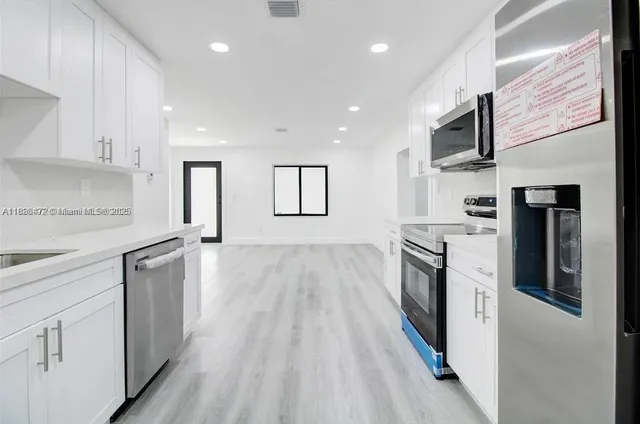 a large kitchen with stainless steel appliances granite countertop a lot of cabinets and wooden floor