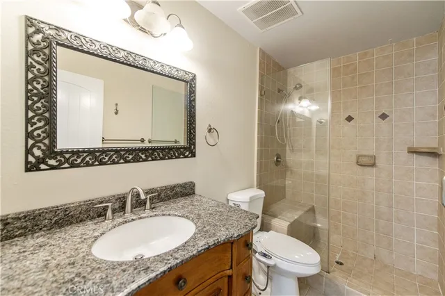 a bathroom with a granite countertop toilet a sink a mirror and shower