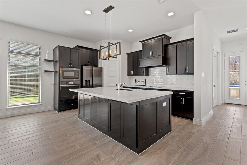 960 Knoxbridge Road Forney, TX 75126 - Photo 5 of 22 Modern kitchen featuring dark cabinetry, stainless steel appliances, a white subway tile backsplash, and a large central island with a white countertop and integrated sink