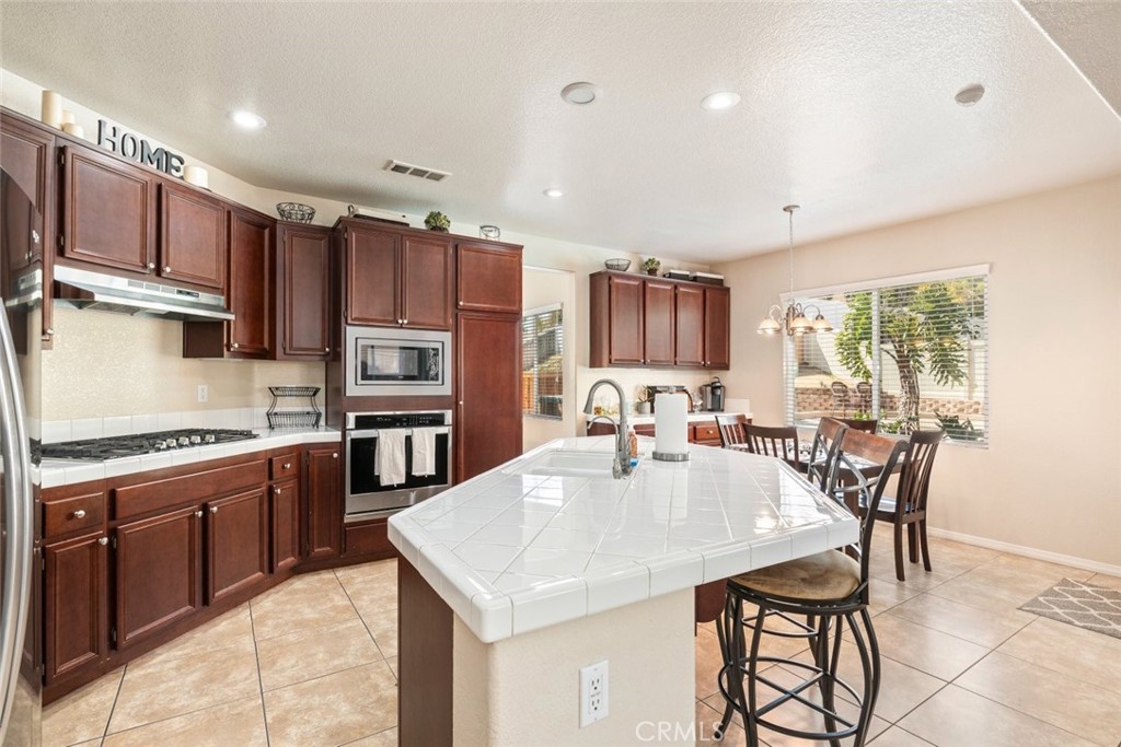 46123 Drymen Avenue Temecula, CA 92592 - Photo 14 of 42 a kitchen with stainless steel appliances granite countertop a stove top oven a sink dishwasher a dining table and chairs with wooden floor