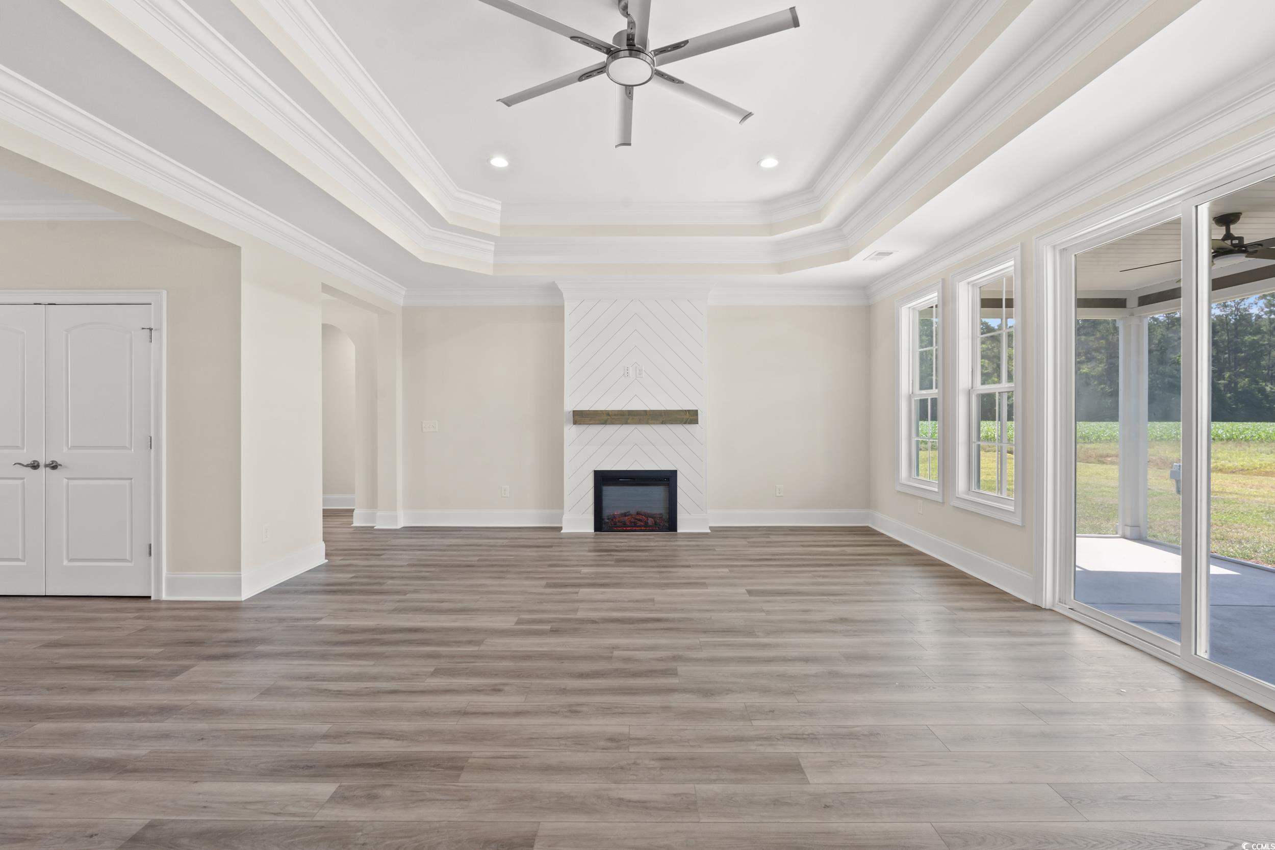 4022 Macks Road Aynor, SC 29511 - Photo 3 of 35 Unfurnished living room with ceiling fan, a tray ceiling, wood finished floors, a large fireplace, and crown molding