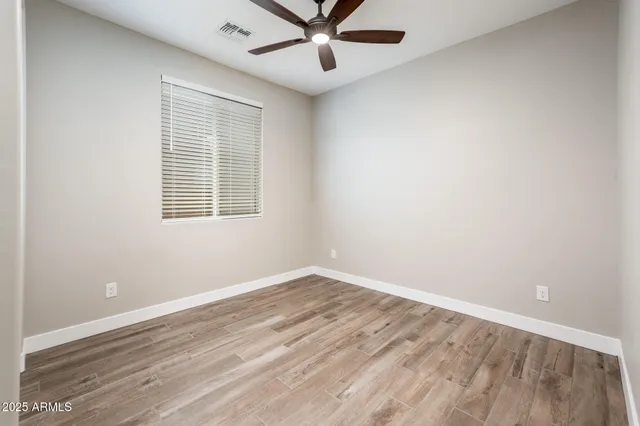 an empty room with wooden floor fan and windows